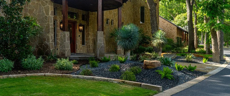 A rock landscape bed in New Braunfels, TX, with plants and purple flowers.